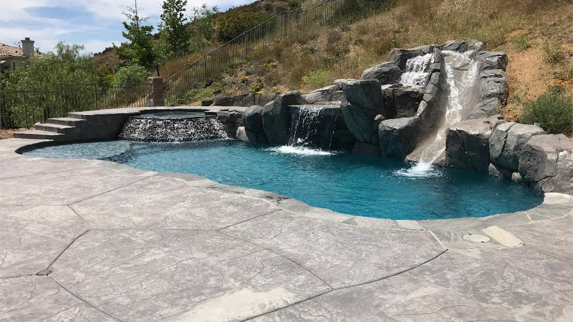 Luxury custom pool with turquoise water, rock waterfall features, and stone patio decking