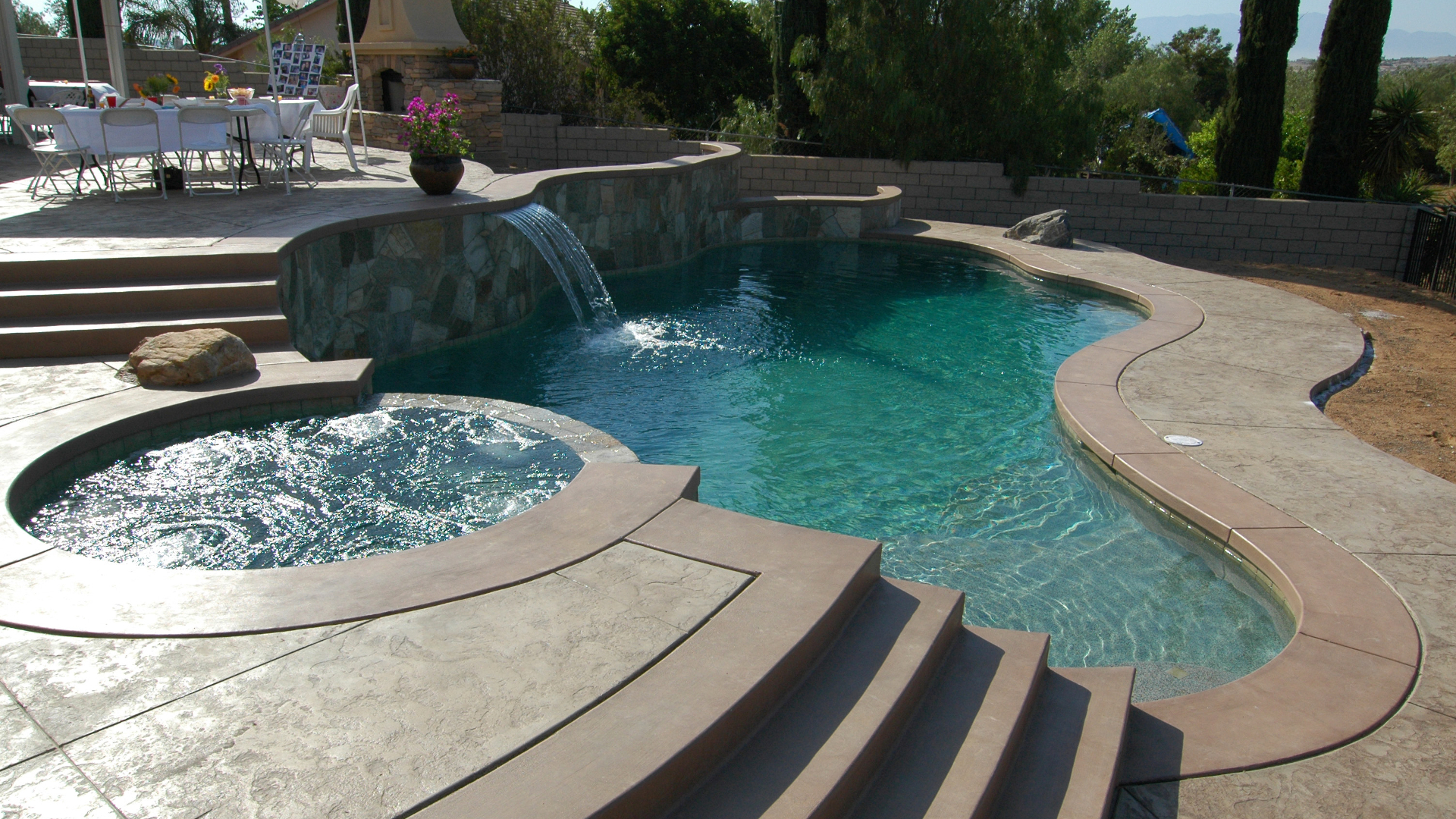 Luxury backyard pool with spa, waterfall feature, and resort-style stone decking overlooking countryside