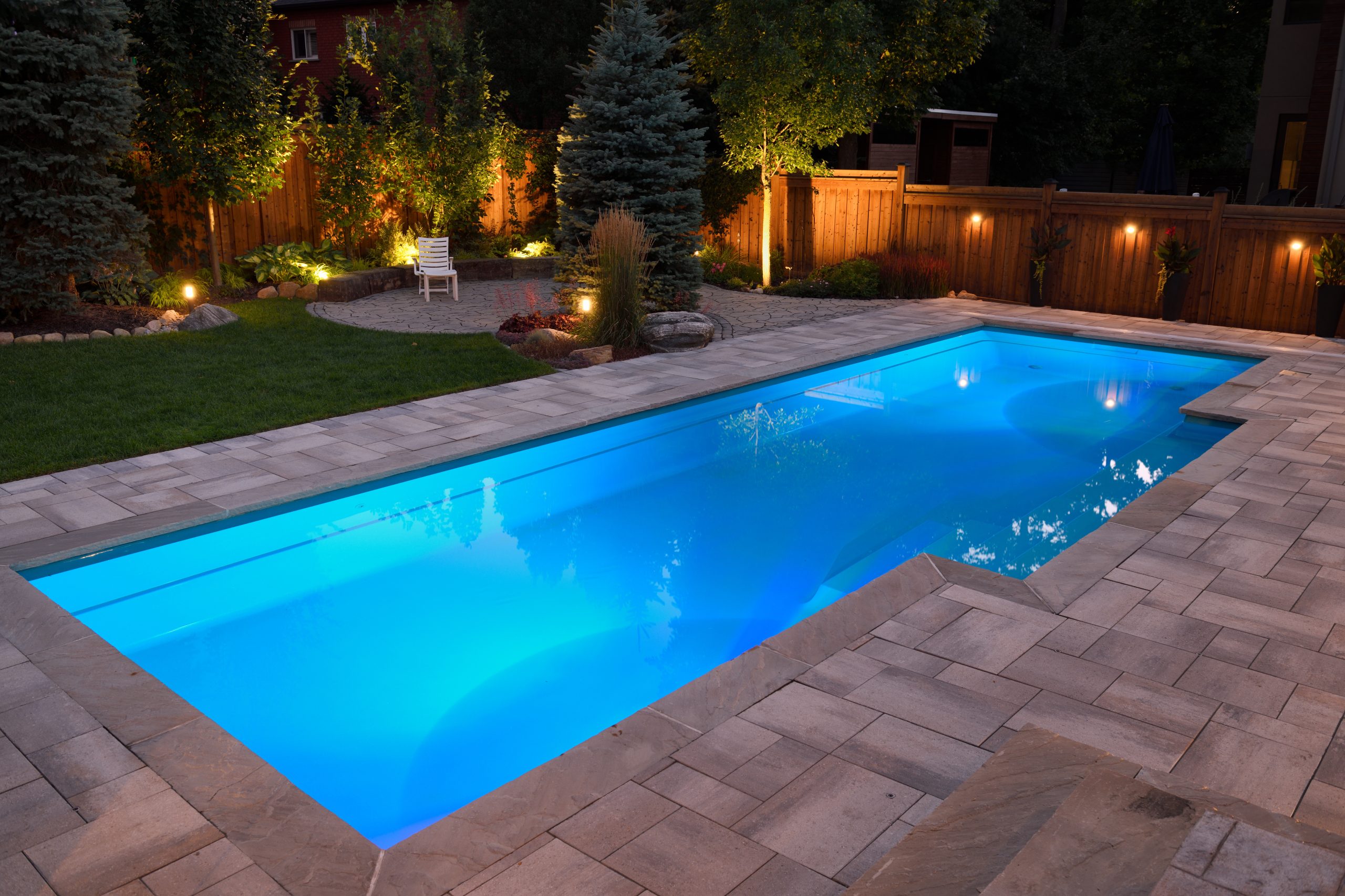 Illuminated luxury backyard pool with custom patio deck and ambient landscape lighting at night